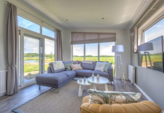 Helles, modernes Wohnzimmer in einer Lodge des Pavilion Poort van Zeeland, mit großen Fenstern und Blick ins Grüne.