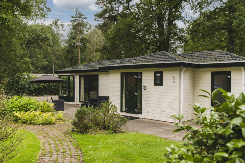 Naturhytte ved Bospark Markelo i Holland, omgivet af grønne planter og træer med terrasseområde.