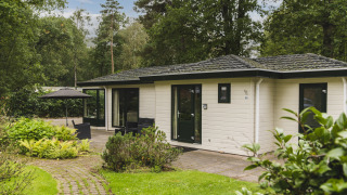 Nature lodge at Bospark Markelo in the Netherlands, surrounded by trees and greenery with patio seating area.
