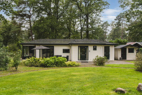 Natuur lodge bij Bospark Markelo in Nederland, omringd door bos en groene tuin met terras.