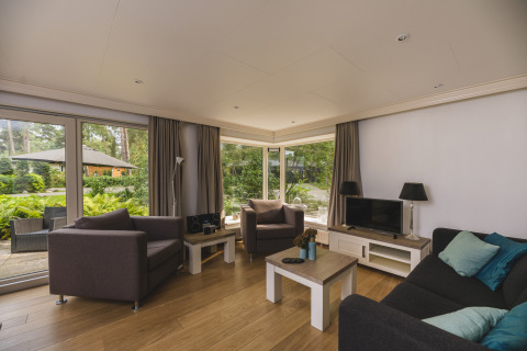 Moderne stue i Nature lodge ved Bospark Markelo, Holland, med store vinduer og haveudsigt.