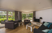 Moderne woonkamer in Nature lodge bij Bospark Markelo, Nederland, met grote ramen en uitzicht op de tuin.