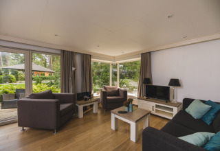 Modern living room in Nature lodge at Bospark Markelo, Netherlands, with large windows and garden view.
