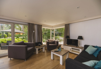 Moderne stue i Nature lodge ved Bospark Markelo, Holland, med store vinduer og haveudsigt.