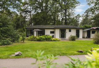 Zicht op de Nature Lodge in Bospark Markelo, Nederland, omringd door grasvelden en groene bomen.