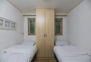 Dormitorio sencillo con dos camas individuales y un armario central en la Nature lodge de Bospark Markelo, Países Bajos.