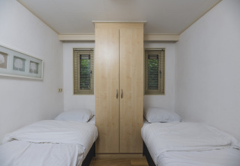 Dormitorio sencillo con dos camas individuales y un armario central en la Nature lodge de Bospark Markelo, Países Bajos.