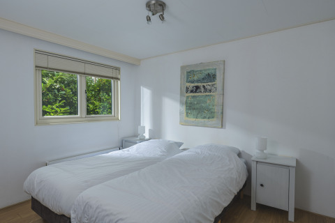 Dormitorio luminoso con dos camas individuales y vistas al jardín en la Nature lodge de Bospark Markelo, Países Bajos.