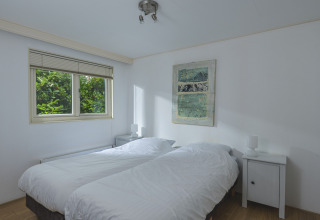 Dormitorio luminoso con dos camas individuales y vistas al jardín en la Nature lodge de Bospark Markelo, Países Bajos.
