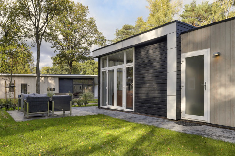 Modern tiny house at Bospark Markelo, Netherlands, with patio seating, green lawn, and surrounding trees.