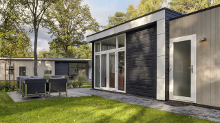 Tiny house moderne à Bospark Markelo aux Pays-Bas, terrasse extérieure, pelouse verte et arbres autour.