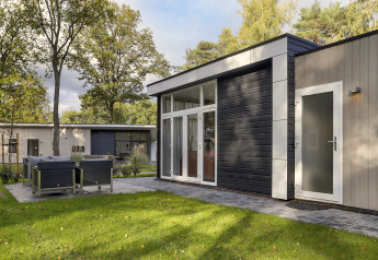 Moderne tiny house op Bospark Markelo in Nederland, met terras, tuinset, grasveld en omringende bomen.