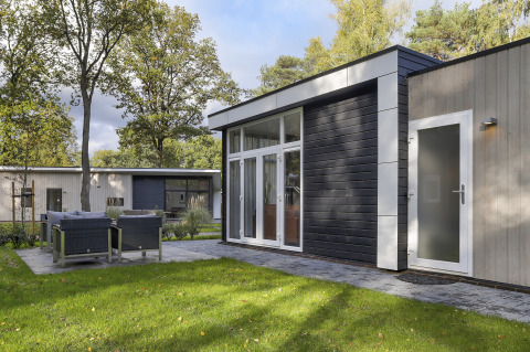 Moderne tiny house op Bospark Markelo in Nederland, met terras, tuinset, grasveld en omringende bomen.