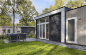 Casa pequeña moderna en Bospark Markelo, Países Bajos, con zona exterior y césped rodeado de árboles.