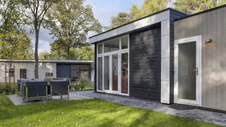 Moderne tiny house op Bospark Markelo in Nederland, met terras, tuinset, grasveld en omringende bomen.