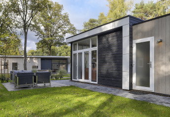 Modern tiny house at Bospark Markelo, Netherlands, with patio seating, green lawn, and surrounding trees.
