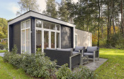 Modernes Tiny House im Bospark Markelo, Niederlande, mit Außensitzbereich in grüner Natur.
