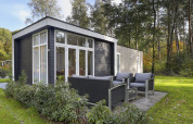 Modernes Tiny House im Bospark Markelo, Niederlande, mit Außensitzbereich in grüner Natur.
