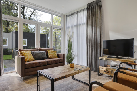 Stilfuld stue i Tiny House på Bospark Markelo, Holland, med store vinduer, sofa og tv.