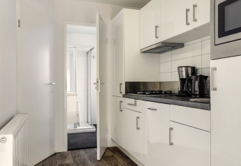 Cuisine moderne de tiny house avec armoires blanches, cafetière, bouilloire et vue sur la salle de bain.
