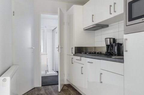 Moderne tiny house keuken met witte kasten, koffiezetapparaat, waterkoker en uitzicht op badkamer.