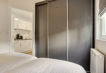Chambre moderne avec armoire grise et vue sur cuisine blanche d'une Tiny House au Bospark Markelo, Pays-Bas.