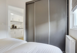 Moderne soveværelse med grå skydedørsgarderobe, udsigt til køkken med hvide skabe i Tiny House i Holland.