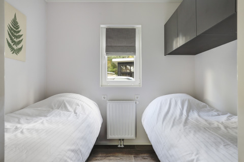 Kleine slaapkamer met twee eenpersoonsbedden, raam en minimalistische stijl in Tiny House bij Bospark Markelo.