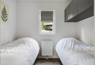 Piccola camera da letto con due letti singoli, finestra e arredi minimal al Tiny House di Bospark Markelo.