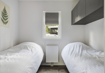 Kleines Schlafzimmer mit zwei Einzelbetten, Fenster und modernen Schränken im Tiny House bei Bospark Markelo.