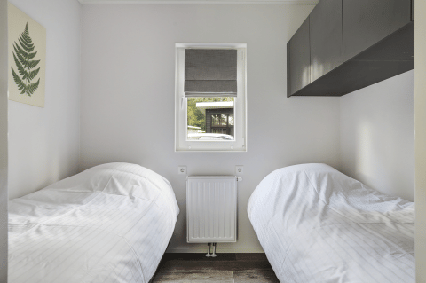 Piccola camera da letto con due letti singoli, finestra e arredi minimal al Tiny House di Bospark Markelo.