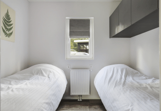Kleine slaapkamer met twee eenpersoonsbedden, raam en minimalistische stijl in Tiny House bij Bospark Markelo.