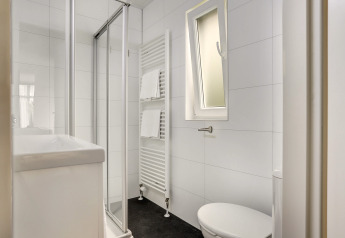 Salle de bains compacte et moderne avec douche, radiateur à serviettes, toilettes et fenêtre à Bospark Markelo.