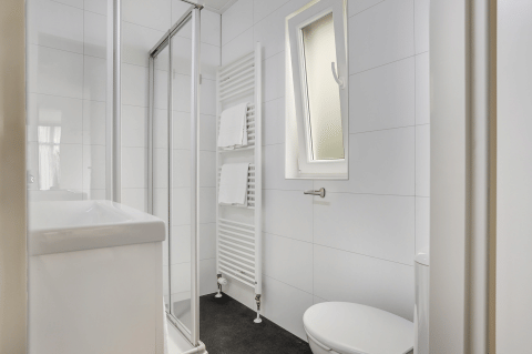Moderne, kompakt badeværelse med brusekabine, håndklæderadiator, toilet og vindue i Tiny House Bospark Markelo.