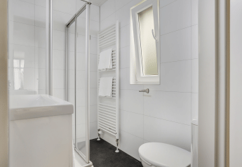 Baño compacto y moderno con ducha, radiador toallero, inodoro y ventana en Tiny House de Bospark Markelo.
