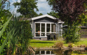 Lille sommerhus Forest Lodge Wellness ved dam, omgivet af grøn natur i Bospark Markelo, Holland.