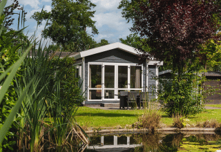 Tiny house Forest Lodge Wellness aan een vijver, omgeven door groen in Bospark Markelo, Nederland.