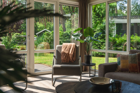 Woonkamer met grote ramen en uitzicht op de tuin in Forest Lodge Wellness, Bospark Markelo, Nederland.