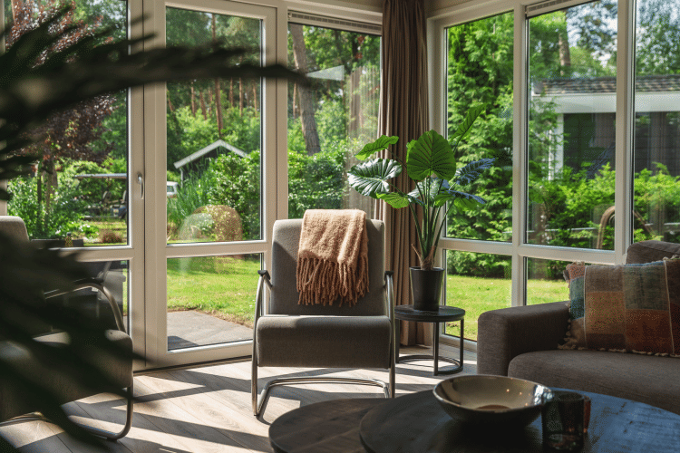 Sala de estar con grandes ventanas y vista al jardín en Forest Lodge Wellness, Bospark Markelo, Países Bajos.