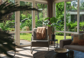 Sala de estar con grandes ventanas y vista al jardín en Forest Lodge Wellness, Bospark Markelo, Países Bajos.