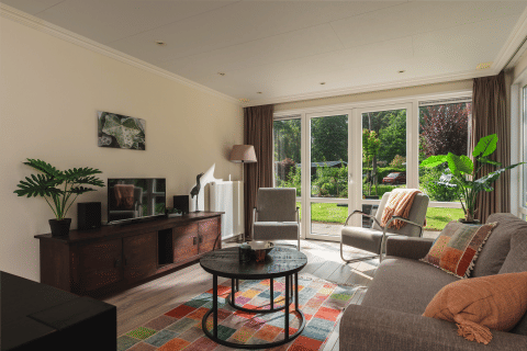 Woonkamer van Forest Lodge Wellness in Bospark Markelo, Nederland, met grote ramen en tuinzicht.