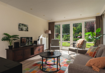 Woonkamer in Forest Lodge Wellness, Bospark Markelo, Nederland, met grote ramen en uitzicht op de tuin.