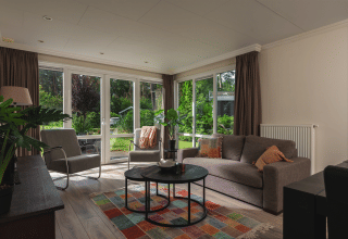 Lichte, moderne woonkamer in Forest Lodge Wellness, Bospark Markelo, met zicht op de groene tuin.