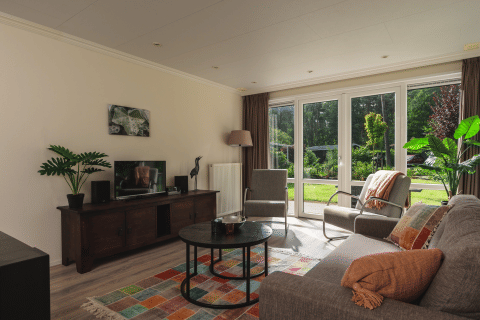 Heldere woonkamer in Forest Lodge Wellness, Bospark Markelo, met grote ramen en kleurrijk tapijt.