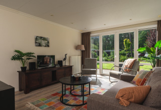 Heldere woonkamer in Forest Lodge Wellness, Bospark Markelo, met grote ramen en kleurrijk tapijt.