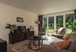 Heldere woonkamer in Forest Lodge Wellness, Bospark Markelo, met grote ramen en kleurrijk tapijt.
