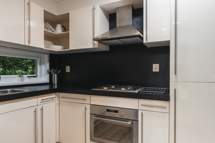 Cocina moderna con encimera negra, estufa de gas, horno y gabinetes blancos en Forest Lodge Wellness, Bospark Markelo.