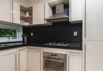 Moderne keuken met zwart werkblad, gaskookplaat, oven en witte kasten in Forest Lodge Wellness, Bospark Markelo.