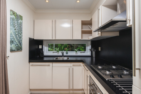 Moderne, compacte keuken in Forest Lodge Wellness, Bospark Markelo, Nederland, met witte kasten en zwart blad.