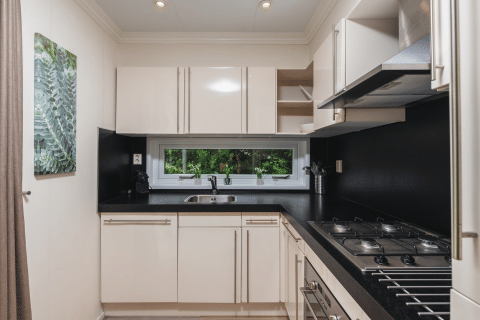 Moderne compacte keuken in Forest Lodge Wellness, Bospark Markelo, Nederland, met witte kasten en zwarte werkblad.